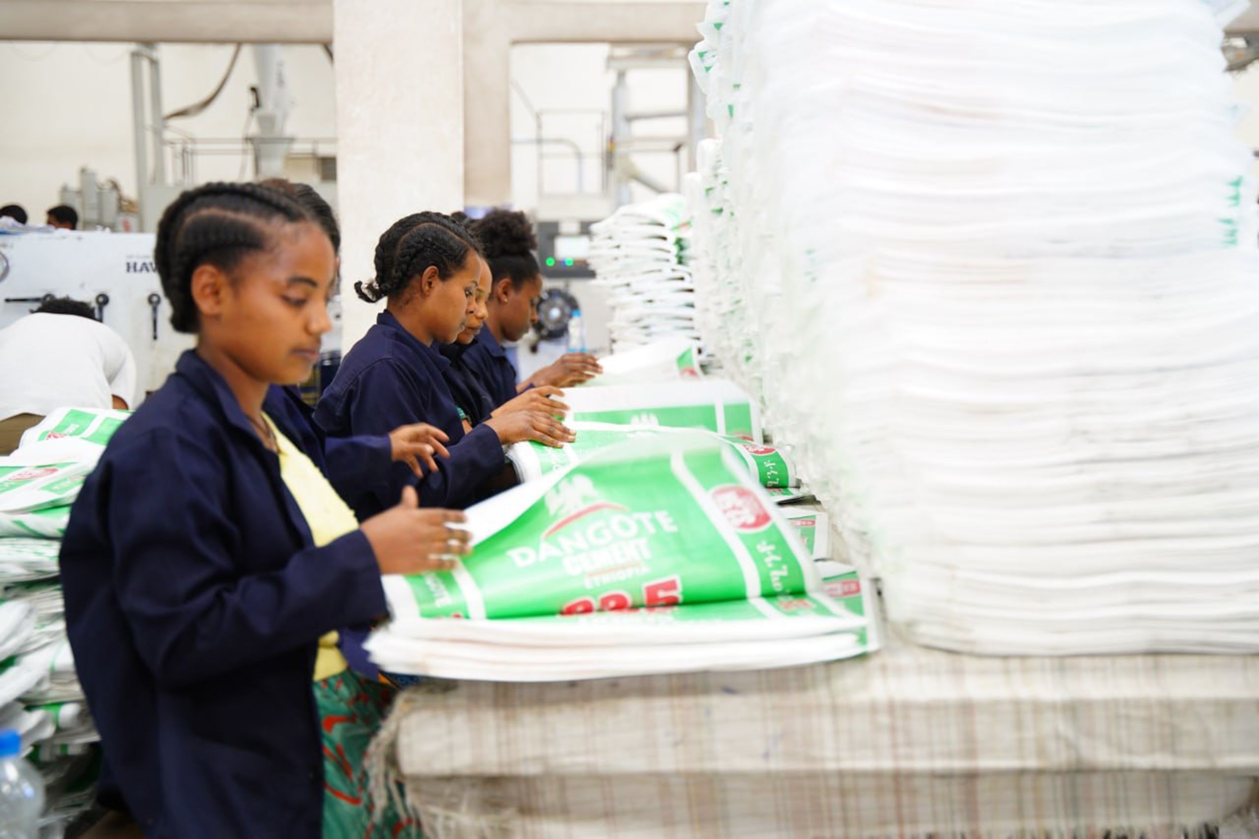 Women in a line sorting white bags with company labels.